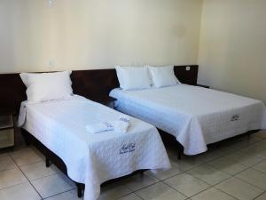 two beds in a hotel room with white sheets at Hotel Monte Carlo Uberaba - Próximo ao Hospital UFTM , Hospital Dr Hélio Angotti e Hospital Regional Uberaba in Uberaba