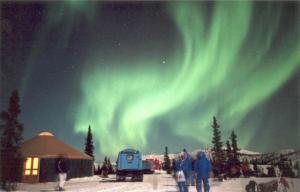 a group of people standing in the snow under the northern lights at Chena Hot Springs Resort in Chena Hot Springs