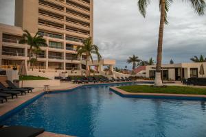 a swimming pool with chairs and palm trees and a building at Ocean View Beach Hotel in Mazatlán
