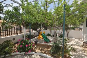 einen Garten mit einem Spielplatz sowie Bäumen und Blumen in der Unterkunft Ocean Village Apartments in Agia Pelagia