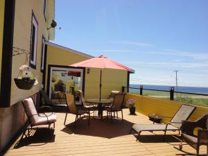 um deque com uma mesa, cadeiras e um guarda-sol em Gîte et Centre de Santé Au Coin De La Berge B&B and Wellness Centre em Percé