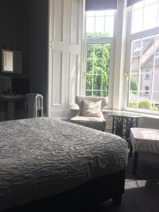 a bedroom with a bed and a chair and windows at Lochnagar Guest House in Aberdeen