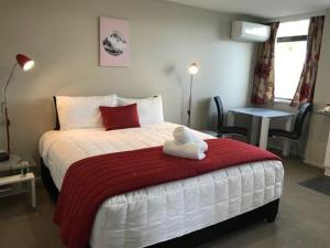 a bedroom with a bed with a red and white blanket at Ascot Oamaru Motel in Oamaru