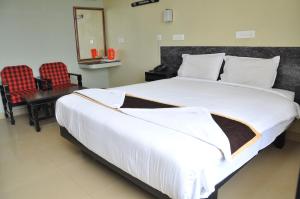 a bedroom with a large white bed with two chairs at Hotel Rajam in Kanyakumari