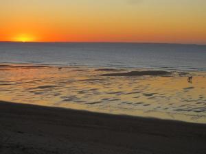 una puesta de sol sobre el océano con gente caminando por la playa en Residence les Goelands, en Jullouville-les-Pins