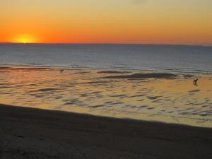 um pôr do sol sobre o oceano com pessoas caminhando na praia em Residence les Goelands em Jullouville-les-Pins