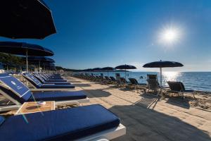 a row of lounge chairs and umbrellas on a beach at Gallia Palace Hotel - Relais & Ch&acirc;teaux in Punta Ala