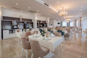 a restaurant with white tables and chairs and a kitchen at Hotel Perla in Rogoznica