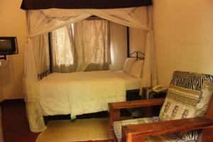 a bedroom with a bed with a canopy and a chair at Kindoroko Hotel in Moshi