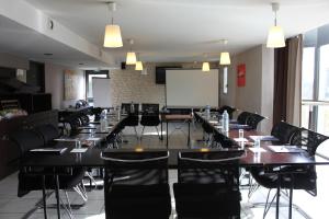 une salle de conférence avec des tables et des chaises et un écran de projection dans l'établissement The Originals City, Hotel Novella Confort, Nantes Est, à Carquefou