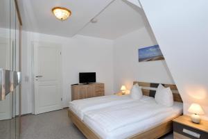 Schlafzimmer mit einem weißen Bett und einem TV in der Unterkunft Wohnung Sylthome in Westerland
