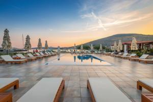 a hotel pool with lounge chairs and a sunset at Marina Baotić Apartments in Trogir