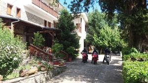 2 personnes voyageant en moto dans une rue à côté d'un bâtiment dans l'établissement Bourazani Wild Life Resort, à Konitsa