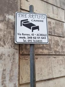 Un cartello su un palo davanti a un muro di The Artists ad Acireale