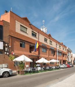 ein Hotel mit Tischen und Sonnenschirmen vor einem Gebäude in der Unterkunft Hotel Vivar in Griñón