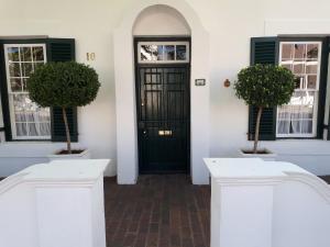 eine Eingangstür eines Hauses mit zwei Topfbäumen in der Unterkunft De Kothuize 10 in Graaff-Reinet