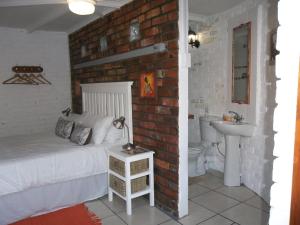 um quarto com uma parede de tijolos, uma cama e um lavatório. em Wiltshire Rondavel em Port Alfred