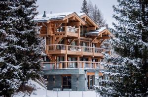une grande maison en bois dans la neige avec des arbres dans l'établissement Chalet Migui Luxury Living & Spa *****, Crans Montana, à Crans-Montana