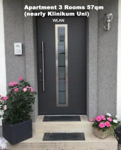 une porte d'entrée noire avec deux plantes en pot et des fleurs dans l'établissement Apartment am Klinikum, à Cassel