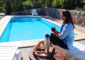 a woman sitting on a chair next to a swimming pool at Cabañas El Arcano in Capilla del Monte