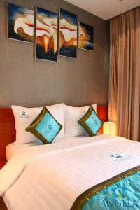 a bedroom with a white bed with paintings on the wall at Angela Boutique Serviced Residence in Ho Chi Minh City