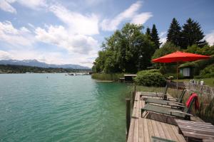 a wooden dock with chairs and an umbrella and water at Villa Christa in Velden am Wörthersee