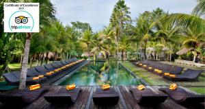 a pool at a resort with lounge chairs and palm trees at The Mansion Resort Hotel & Spa in Ubud