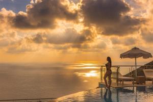 a woman standing on the edge of a pool with the ocean at Petani Bay Hotel - Adults Only in Vóvikes