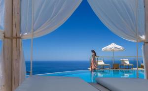 a woman standing next to a swimming pool with an umbrella at Petani Bay Hotel - Adults Only in Vóvikes