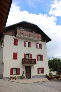 a white building with red shutters and a balcony at Durmi e Insumiasci in Forni Avoltri