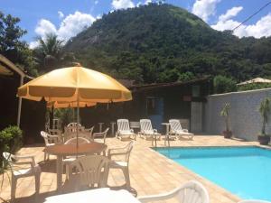 a table and chairs with an umbrella next to a swimming pool at Pousada Nascente Pequena in Guapimirim