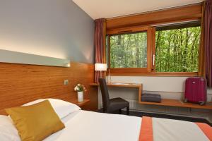 a hotel room with a bed and a desk and a window at H&ocirc;tel Centre Port-Royal in Saint-Lambert