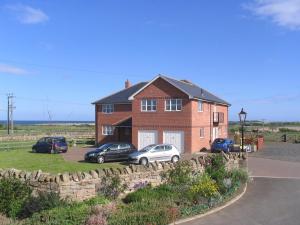 uma casa de tijolos com carros estacionados em frente em Springwood em Seahouses