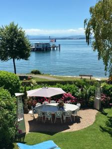 einen Tisch mit Stühlen und einen Regenschirm neben dem Wasser in der Unterkunft Boutique Hotel Villa am See in Hagnau