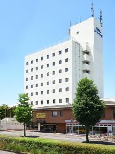 un gran edificio blanco con árboles delante de él en Hotel Route Tsukuba, en Tsukuba