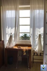 a desk in front of a window with white curtains at Hotel Mimosa in Spotorno