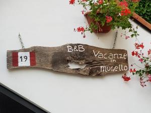 ein Holzschild hängt an einer Wand mit Blumen in der Unterkunft B&B Vacanze in Mugello in San Piero a Sieve