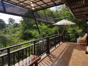 a balcony with an umbrella and a table and chairs at Kaengkrachan River Hut in Kaeng Krachan