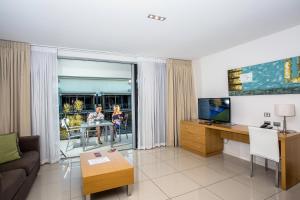 Ramada by Wyndham Hervey Bay في خليج هيرفي: غرفة معيشة مع أريكة وتلفزيون وطاولة