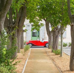 une voiture rouge garée devant une maison arborée dans l'établissement Cerise Carcassonne Sud, à Carcassonne