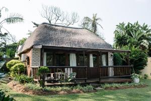 een rieten dakhuis met een veranda en een terras bij African Sands B&B in Amanzimtoti
