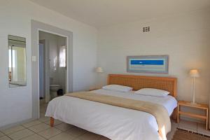 Un dormitorio con una cama grande con sábanas blancas. en Roman Rock Apartments, en Simonʼs Town