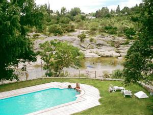 a person sitting next to a swimming pool next to a river at Costa Serrana Apart Hotel in Mina Clavero