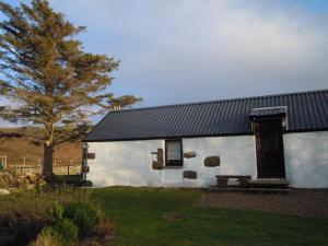 a white house with a black roof and a tree at The Smithy House & Cottages in Lochinver