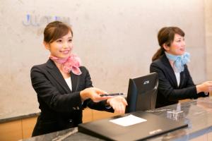 dwie kobiety w garniturach siedzące przy stole z laptopem w obiekcie Just Inn Premium Nagoya Station w mieście Nagoja