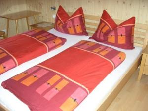 Duas camas com almofadas vermelhas e laranja num quarto em Appartement Bischof em Schoppernau