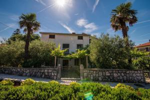 une maison avec des palmiers et un mur en pierre dans l'établissement Apartments Maestral, à Malinska