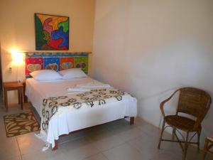 a bedroom with a bed and a chair and a painting at Pousada Araçás Village in Imbassai