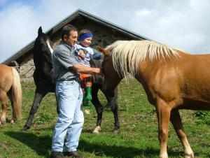 Um homem está a acariciar um cavalo castanho com uma rapariga. em Agritur Dalaip dei Pape em Fiera di Primiero