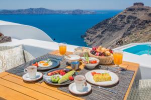 フィロステファニにあるシック ホテル サントリーニの海を見渡すテーブルの上に食べ物と飲み物を用意した朝食用テーブル